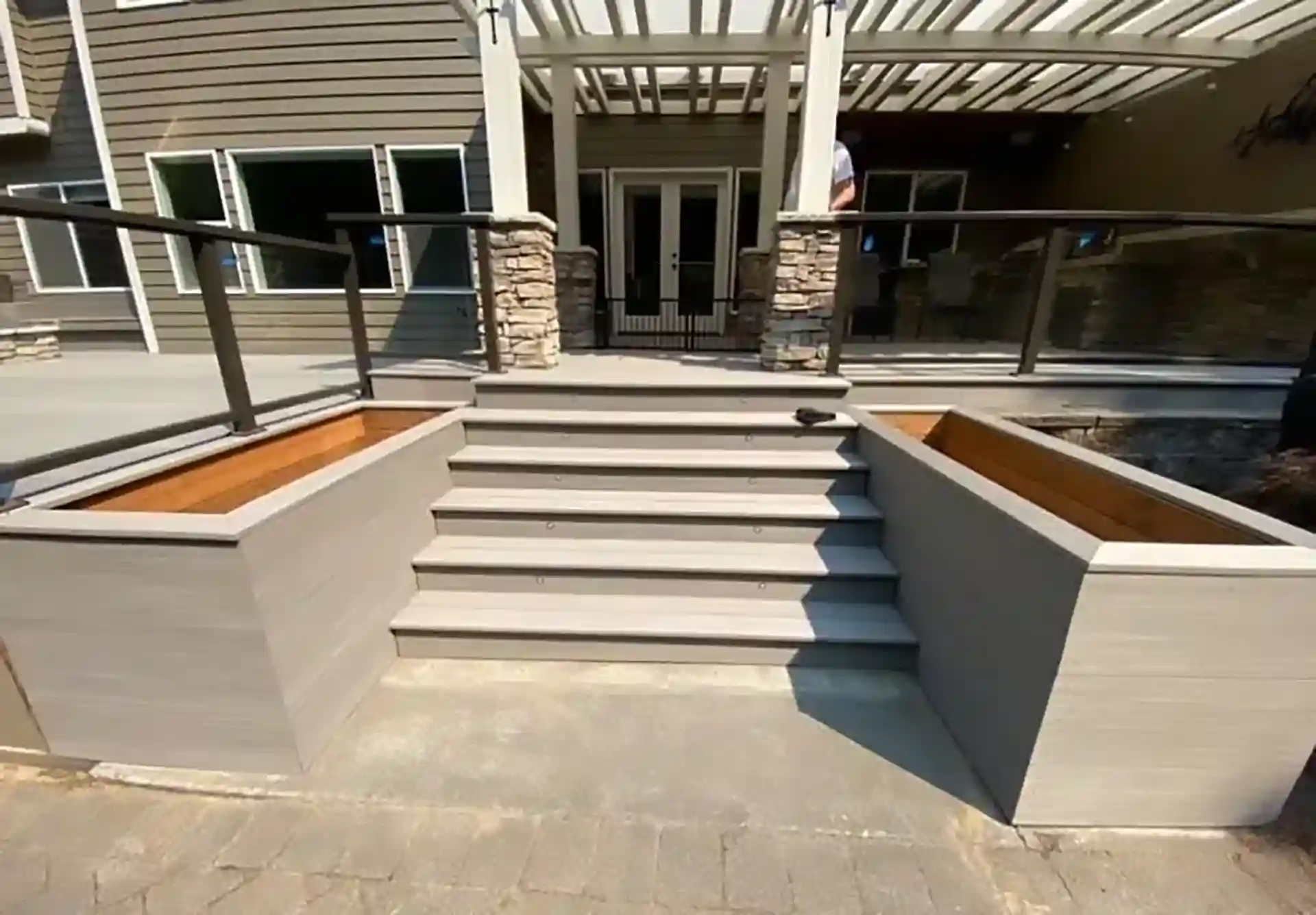 Patio with steps leading up to a raised deck with pergola - Patio Builders Near Me - Custom Concrete Patio Contractors